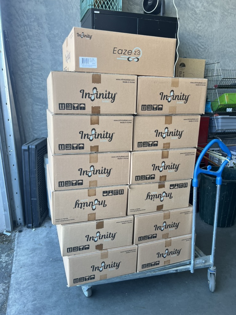 Stack of Infinity Bidet boxes, including an Eaze Z3, on a hand cart, ready to ship