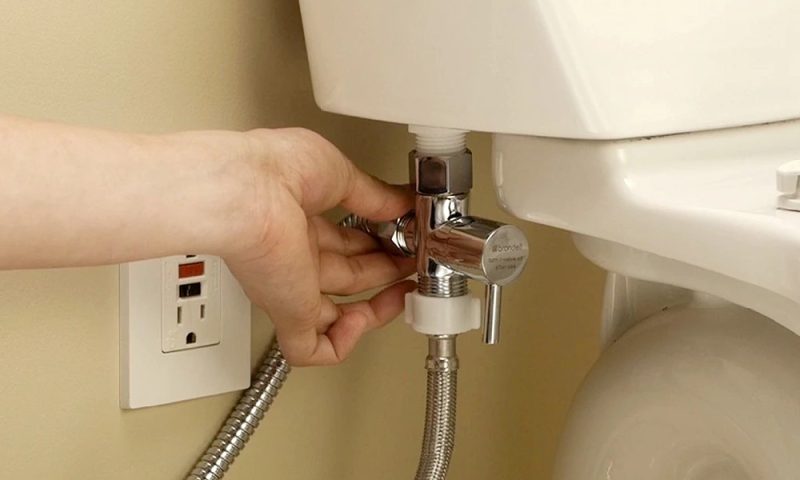 Hand tightening the water supply valve behind a toilet during a bidet installation